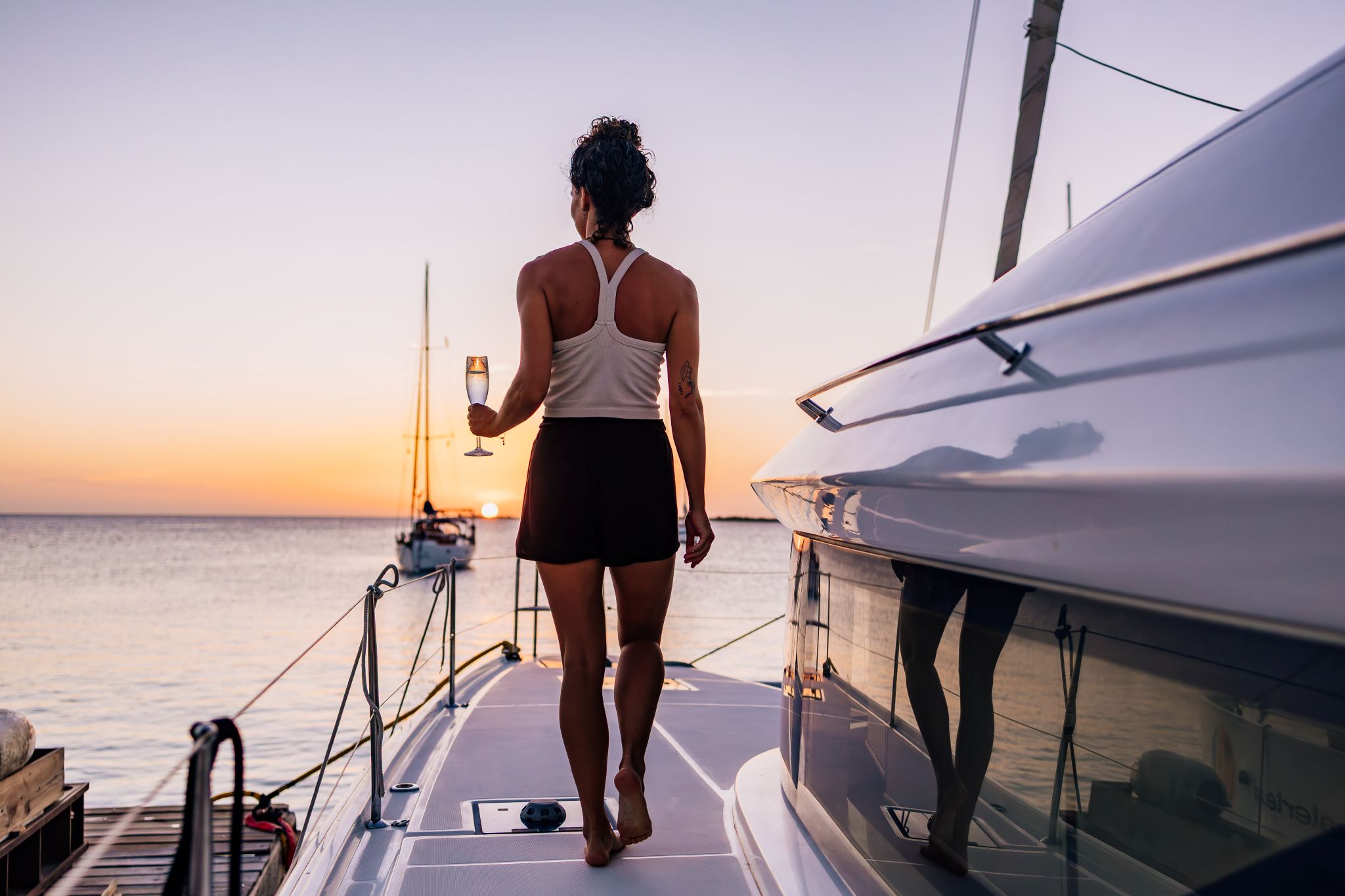 guest walking the bow of private catamaran charter at sunset with a glass of champagne