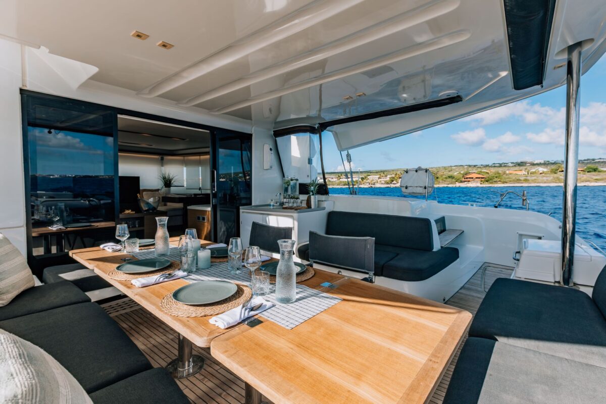 Aft deck dining area aboard a private catamaran charter with salon and coastline view